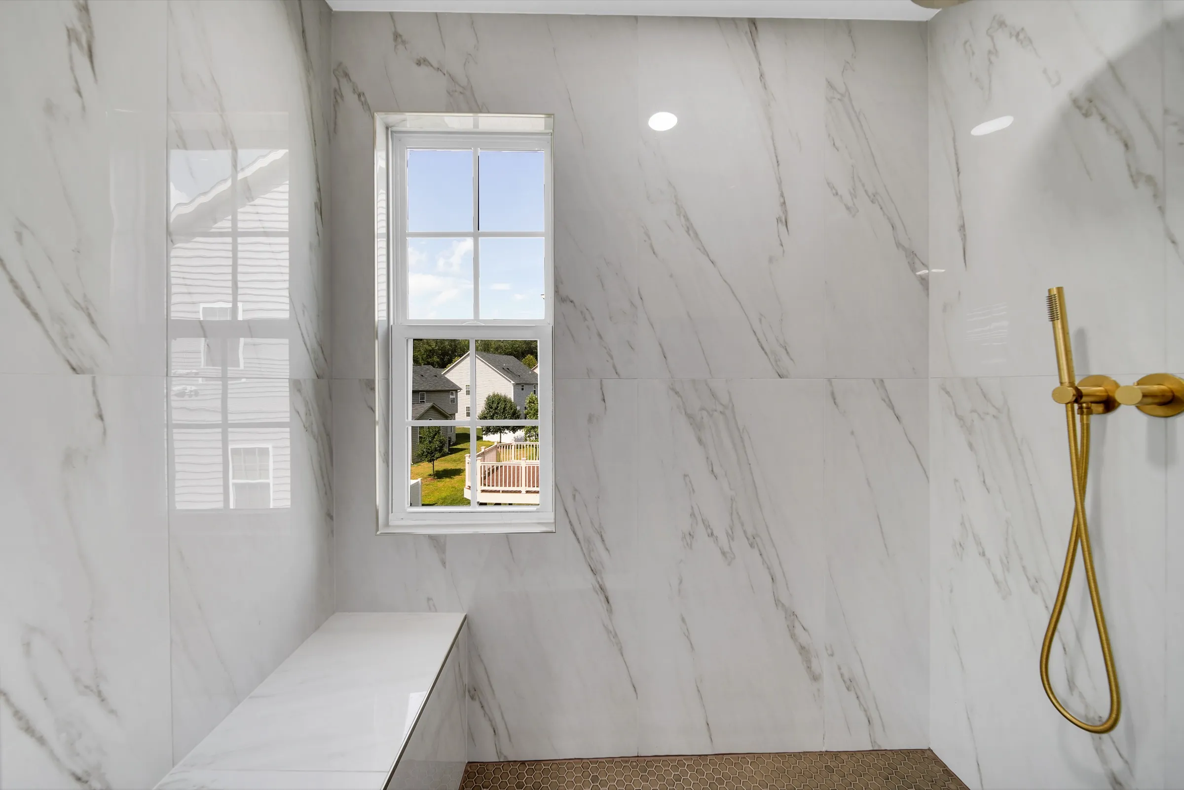 Walk-in shower with marble-look walls, a bench, a window and brushed gold fixtures