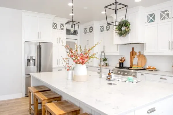 After: a white kitchen with shaker cabinets, a large white island and lantern pendants